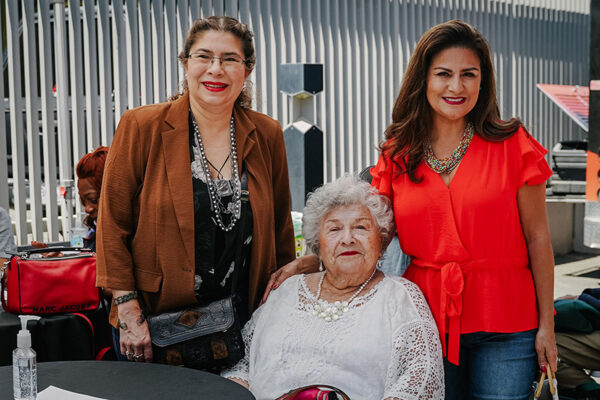Three women, two adults standing up behind an more elderly lady sitting down