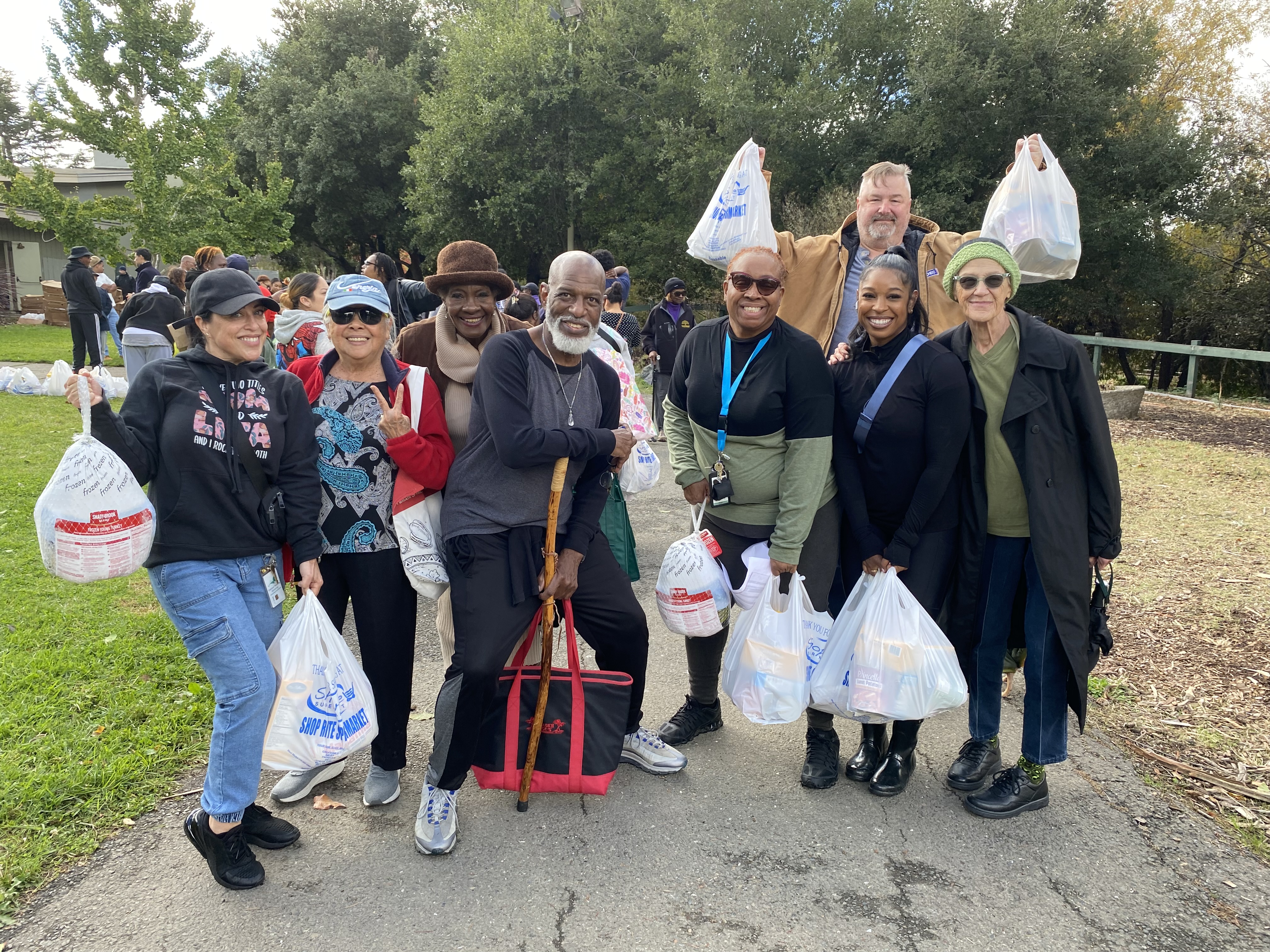 Alt Text: A group of OHA staff and residents smiling while holding holiday meal bags at the District 6 Thanksgiving Food Giveaway.