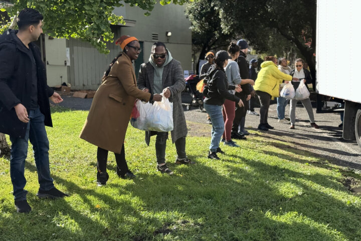 Oakland Housing Authority staff and volunteers form a line to unload bags of food from a truck and distribute them to residents during a Thanksgiving community food drive in November 2024.