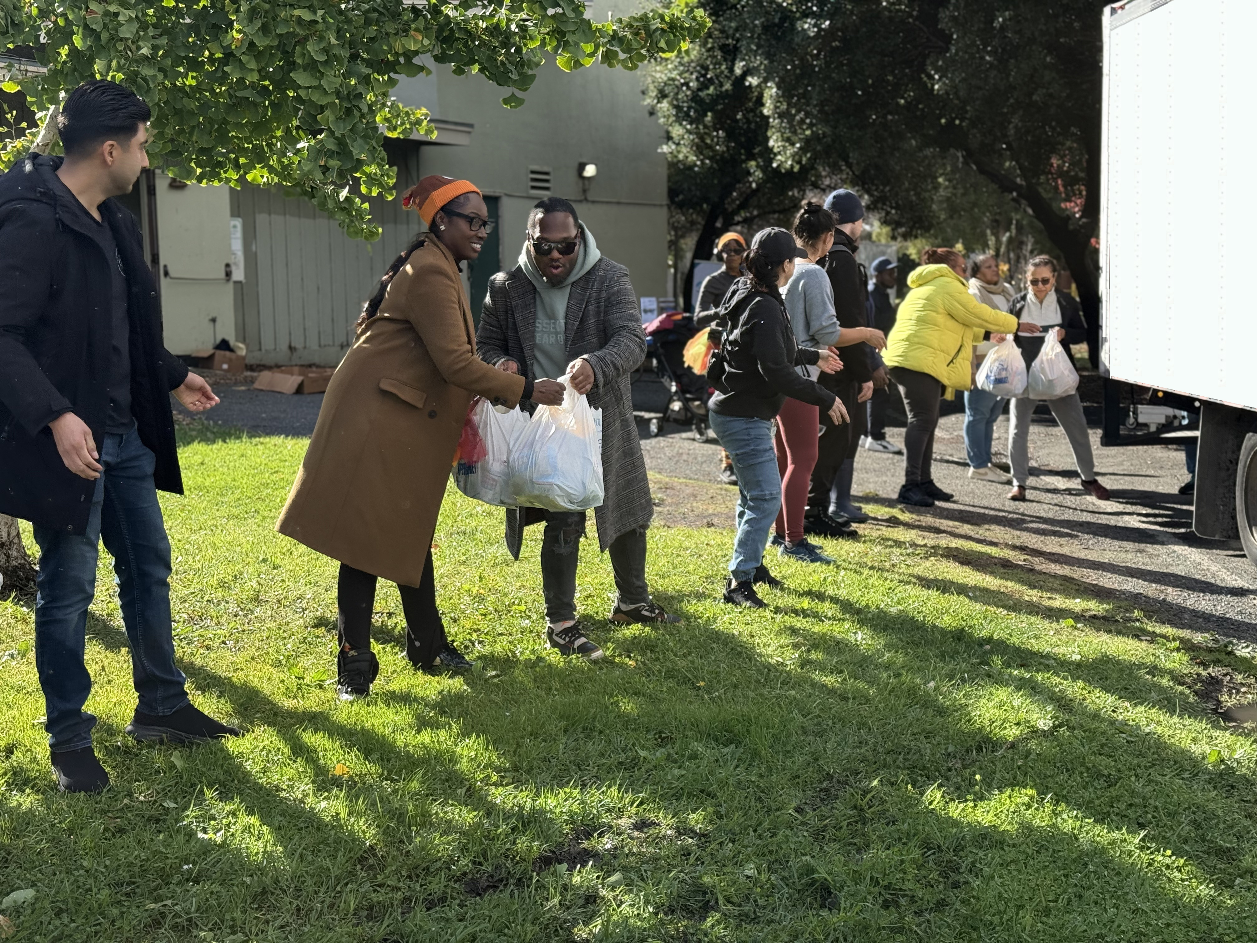 Oakland Housing Authority staff and volunteers form a line to unload bags of food from a truck and distribute them to residents during a Thanksgiving community food drive in November 2024.