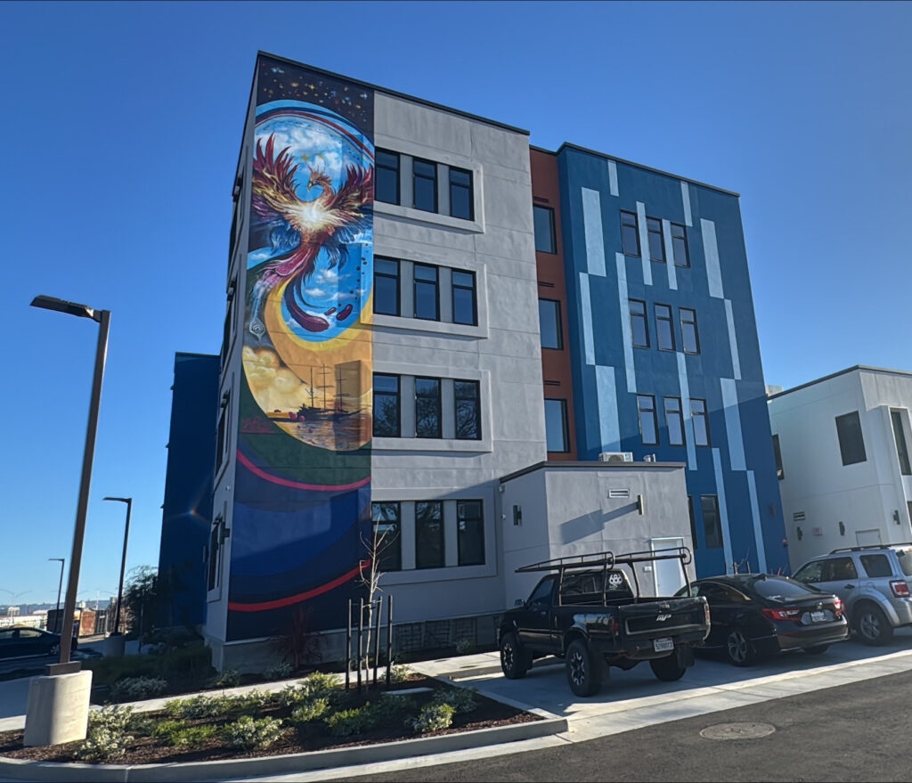 Exterior of The Phoenix affordable housing community in West Oakland featuring a large colorful mural on the building.