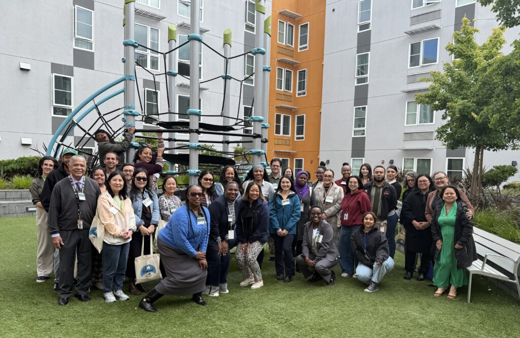 Affordable Housing Month bus tour participants gather near a playground in the courtyard at Jack London Gateway Apartments.