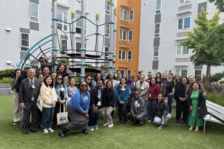 Affordable Housing Month bus tour participants gather near a playground in the courtyard at Jack London Gateway Apartments.