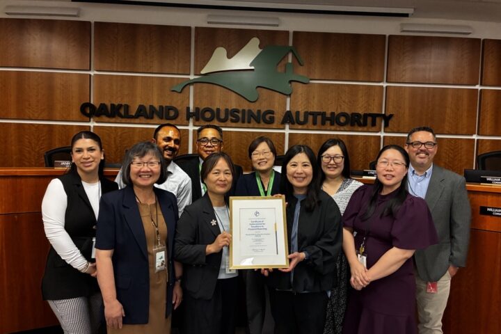 The Oakland Housing Authority (OHA) Finance team members hold the Government Finance Officers Association (GFOA) Certificate of Achievement in the OHA Board of Commissioners Room.