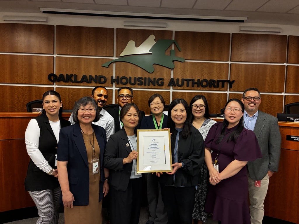 The Oakland Housing Authority (OHA) Finance team members hold the Government Finance Officers Association (GFOA) Certificate of Achievement in the OHA Board of Commissioners Room.
